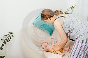 Mother putting clothes on her newborn baby on the chair