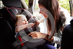 Mother Putting Daughter In Safety Seat On Car Journey