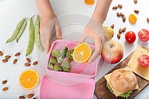 Mother putting food for schoolchild in lunch box on table