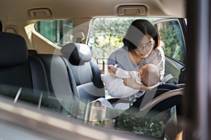 mother putting her little baby son into car seat