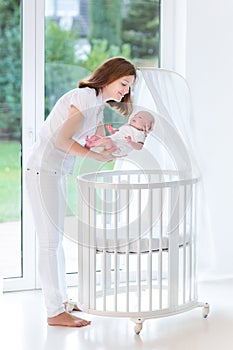 Mother putting her newborn baby to sleep in crib