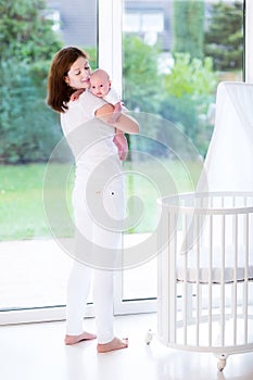 Mother putting newborn baby in bed next to window