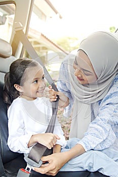 Mother putting on seat belt for her daughter