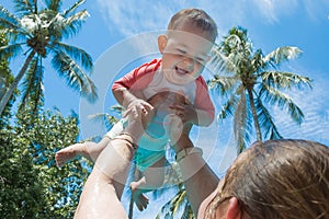 Mother raised up infant child high above the head in the pool. The little baby girl is very happy and screams for joy. Summer