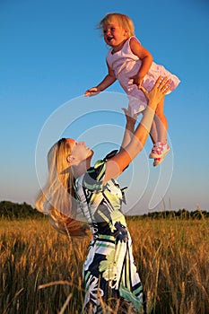 Mother raises child on hands in wheaten field