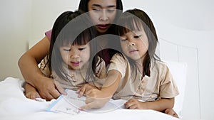 Mother reading bedtime stories to child before putting her daughters to sleep. Happy family time.