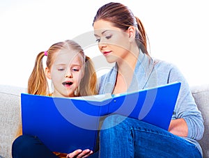 Mother reading book with daughter at home.