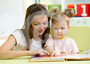 Mother reading book her kid daughter at table