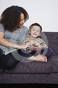 Mother reading book with son (5-6) on sofa