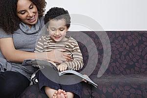 Mother reading book with son (5-6) on sofa