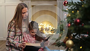 Mother reading book to daughter near xmas tree.