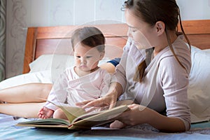 Mother reading a book to her child on the bed. Bedtime story. Learning how to read.