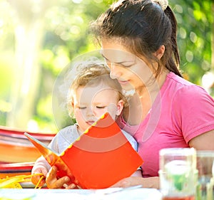 Mother reading a book to her little baby in sunny park