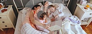 Mother reading book to her sons in the bed