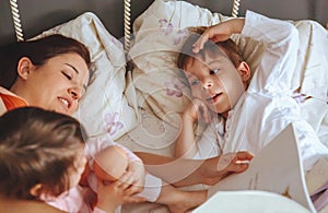 Mother reading book to her sons in the bed