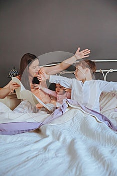 Mother reading book to her sons in the bed