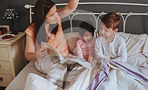 Mother reading book to her sons in the bed