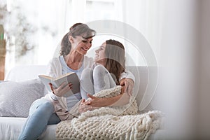 Mother reading book to smiling daughter while relaxing at home