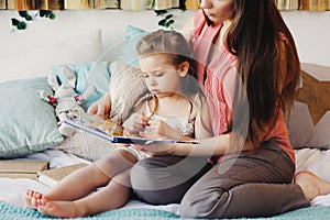 Mother reading book to toddler daughter in bedroom for good night