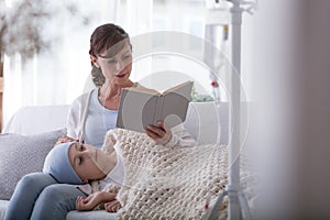 Mother reading book to weak child with leukemia