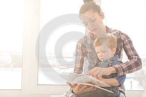 Mother reading with her son on a background of the window