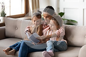 Mother reading interesting fairy tale story book to little daughters