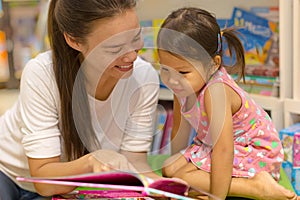 Mother reading a story book to her child at the library. Kids learning how to read