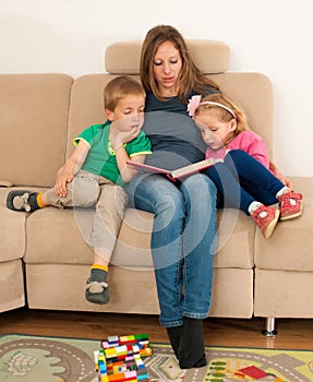 Mother reading a story book to her cildren on a couch in living