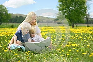 Mother Reading Story Book to Two Young Children Outside in Meadow