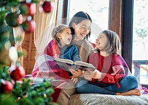 Mother reading to daughters near Christmas tree