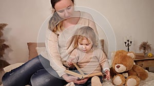 A mother reads a book with her daughter. A woman and a girl play, laugh, leaf through the pages. Love caring home comfort family e