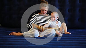 Mother reads a book to a baby sitting on a mattress
