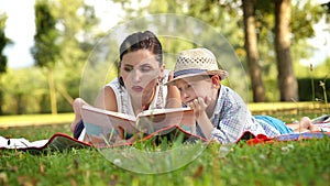 Mother reads a book to her son in the park lying on the rug