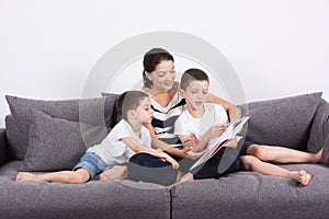 Mother reads an interesting book with her sons of the sofa.