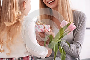 Mother receiving gift and flowers from her cute little daughter at home