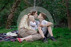 Mother resting with two children in nature. Family picnic in Park. Mom kisses son