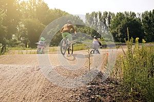 A mother rides bike together with her two daughters on a bicycle dirt track in bright summer light