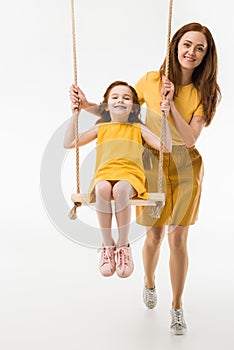 Mother riding happy little daughter on swing