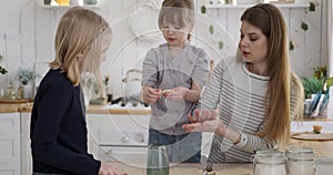 Mother rolling dough and guiding daughters in making biscuits