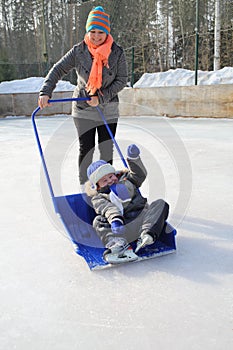 Mother rolls small son in a large snow shovel on a