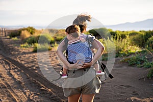 Mother running while carrying a baby on her back in a baby carrier outdoors