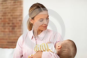 Mother's care. Loving mom holding her little sleeping baby daughter on hands and lulling her, sitting on bed at home