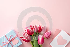 Top view photo of bouquet of fresh tulips blue giftbox pink envelope and postcard with heart on pastel pink background