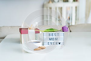 Mother`s day background. Morning suprise - cup of tea with cookies, gift box, lightbox with words Best mom ever and tulip flower