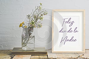 Mother`s day card in Spanish in a wooden frame next to some flowers in a jar. Empty copy space