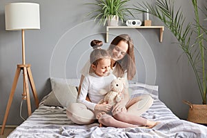 Mother's day. Caucasian mother and daughter sitting in bed woman hugging her cute child smiling