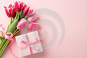 Top view photo of giftbox with ribbon bow and bouquet of pink tulips on isolated pastel pink background with copyspace