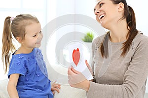 Mother`s day concept. Child daughter congratulates mom and gives her postcard with red heart shape. Mum and girl happy