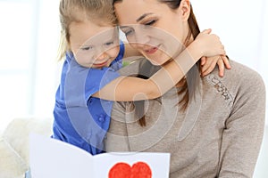 Mother`s day concept. Child daughter congratulates mom and gives her postcard with red heart shape. Mum and girl happy