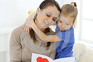 Mother`s day concept. Child daughter congratulates mom and gives her postcard with red heart shape. Mum and girl happy